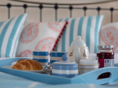 A tray with a croissant, cups, a teapot, and a jar of jam on a bed with striped and patterned pillows at Flaad House in Rock