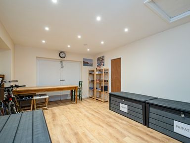 A room with wooden flooring a long table two large storage boxes bicycles and a wooden shelf at Flaad House in Rock