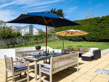An outdoor patio with a wooden dining table set under a blue umbrella and a beige sectional sofa under a beige umbrella at Flaad House in Rock