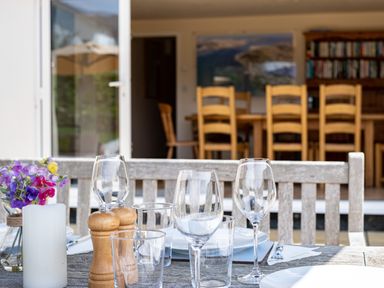 A dining table set with glasses plates and cutlery outside a room with wooden chairs and a bookshelf at Flaad House in Rock