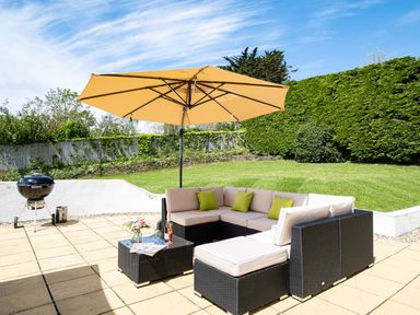 An outdoor patio with a corner sofa set under a large umbrella a charcoal grill and a grassy garden at Flaad House Rock