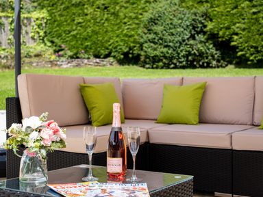 An outdoor seating area with a beige sectional sofa with green cushions a glass table with a bottle of champagne two glasses a vase with flowers and magazines at Flaad House in Rock