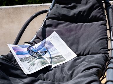 A black cushioned chair with an open magazine and sunglasses resting on it outdoors