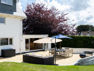 An outdoor patio with a sectional sofa, dining table with chairs, umbrellas, and a barbecue grill at Flaad House in Rock