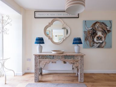 A wooden table with two blue lamps and a basket underneath a mirror and a painting of a cow at Flaad House in Rock