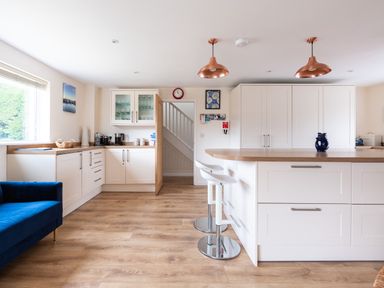 A kitchen with white cabinets wooden countertop two white bar stools and a blue sofa at Flaad House in Rock