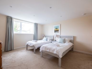 A bedroom with two single beds, bedside tables with lamps, a window with curtains, and a framed picture on the wall at Flaad House in Rock