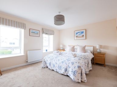 A bedroom with a bed with floral bedding two bedside tables with lamps two windows with striped blinds and framed pictures on the walls at Flaad House in Rock