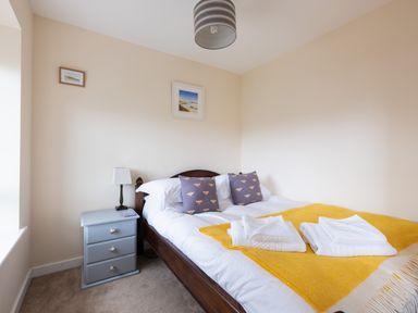 A bedroom with a double bed two purple cushions a yellow blanket and a grey bedside table with a lamp at Flaad House Rock