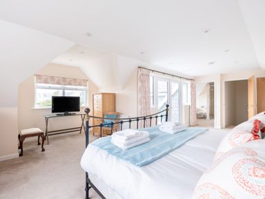 A bedroom with a bed, TV on a glass table, wooden dresser, chair, and windows with curtains at Flaad House in Rock