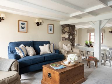 A living room with a blue sofa beige armchair wooden coffee table and dining table at Swallow Cottage in Port Isaac