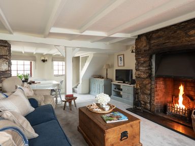 A living room with a blue couch a wooden coffee table a stone fireplace and a dining table at Swallow Cottage Port Isaac