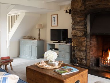 A living room with a stone fireplace a wooden coffee table a television and blue cabinets at Swallow Cottage in Port Isaac