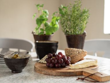A table with grapes cheese seeded bread and a bowl of olives with potted herbs in the background at Swallow Cottage in Port Isaac