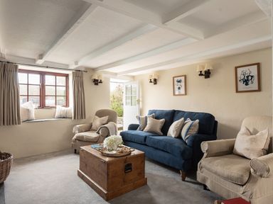 A living room with a blue sofa two beige armchairs a wooden chest as table and a window seat at Swallow Cottage in Port Isaac