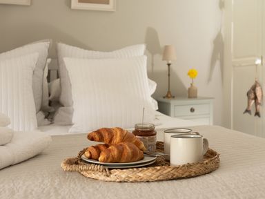 A bed with white pillows and a tray holding croissants jam and two mugs at Swallow Cottage in Port Isaac