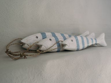 Three wooden fish wall decorations with blue stripes and rope hanging on a textured white surface at Swallow Cottage in Port Isaac