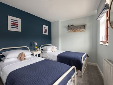 A bedroom with two single beds with blue bedspreads a nightstand in between and a window on the right at Swallow Cottage in Port Isaac