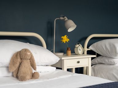 A bedroom with two beds a bedside table with a lamp a clock and a flower at Swallow Cottage in Port Isaac