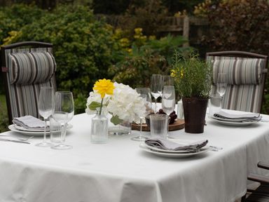 An outdoor dining table set with plates glasses napkins and vases with flowers in a garden at Swallow Cottage in Port Isaac