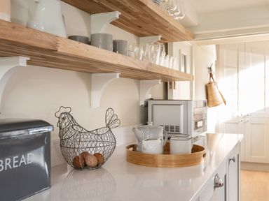 A kitchen counter with a wire chicken egg basket bread box teapot mugs and a microwave at Swallow Cottage in Port Isaac