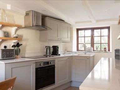 A kitchen with gray cabinets a stainless steel oven and toaster a kettle coffee machine and a window at Swallow Cottage in Port Isaac