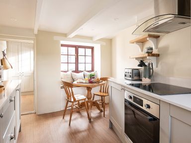 A kitchen with wooden chairs and a small round table near a window with cushions at Swallow Cottage in Port Isaac