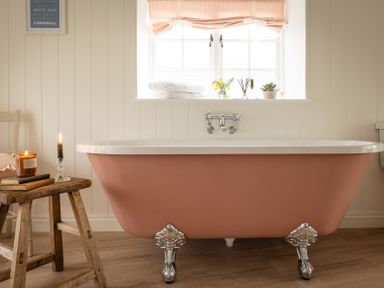 A bathroom with a pink clawfoot bathtub candles books and towels by a window at Swallow Cottage in Port Isaac