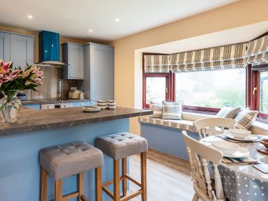 A kitchen with grey bar stools at a counter and a window seat with striped cushions at Brookside in Polzeath