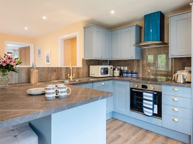 A kitchen with blue cabinets and a marble countertop with mugs and plates at Brookside in Polzeath