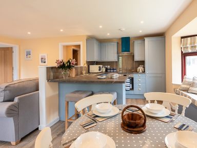 A kitchen and dining area with blue cabinets a dining table set and a couch at Brookside in Polzeath