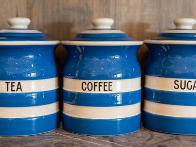 Three blue and white striped kitchen canisters labeled tea coffee and sugar on a countertop