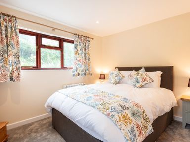 A bedroom with a double bed with leaf patterned cushions and throw near a window at Brookside Polzeath
