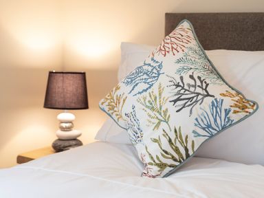 A bedroom with a decorative pillow on a bed and a lamp on a bedside table at Brookside in Polzeath