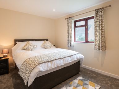 A bedroom with a bed two patterned cushions patterned curtains a bedside table with a lamp and a rug on the floor at Brookside in Polzeath
