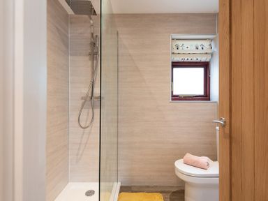 A bathroom with a walk-in shower a toilet with a pink towel on top and a small window at Brookside in Polzeath