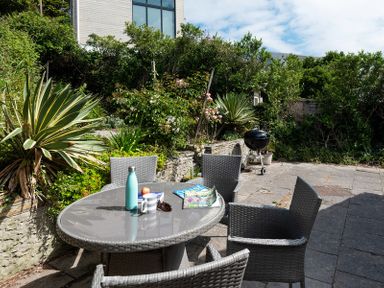 An outdoor patio with a round table and four chairs with plants and a barbecue grill at Brookside in Polzeath