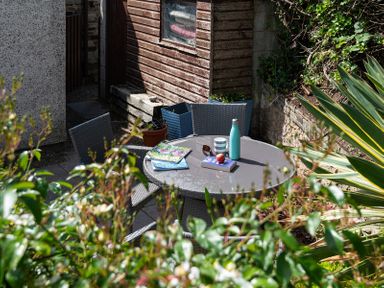 A garden patio with a round table and chairs with books a mug and a water bottle at Brookside in Polzeath
