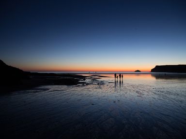 A beach at sunset with three people walking on wet sand near the shore at Brookside in Polzeath