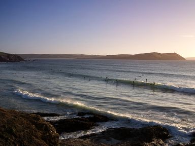 Surfers on waves in the sea near a rocky coastline at Brookside in Polzeath