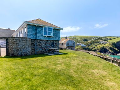A house with stone walls and a small grassy yard near cliffs and the ocean at Gulland in Port Isaac