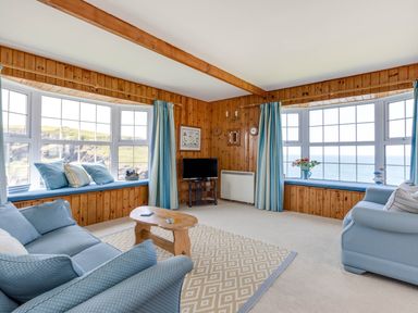 A living room with blue sofas wooden walls bay windows and a small wooden coffee table at Gulland in Port Isaac