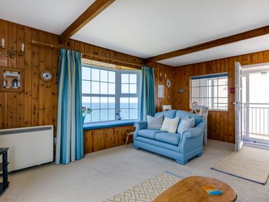 A living room with wood panel walls a blue sofa and large windows overlooking the sea at Gulland in Port Isaac
