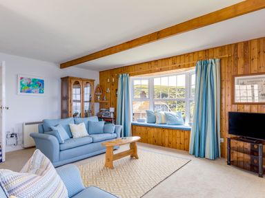 A living room with blue sofas a wooden coffee table and a bay window with cushions at Gulland in Port Isaac
