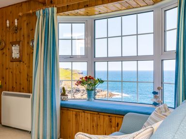 A seating area with a window bench and flowers overlooking the sea at Gulland in Port Isaac
