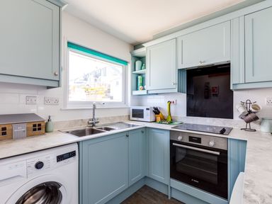 A kitchen with a washing machine microwave oven stovetop and blue cabinets at Gulland in Port Isaac