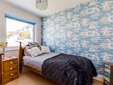 A bedroom with a wooden bed a blue boat patterned wallpaper and a window at Gulland in Port Isaac