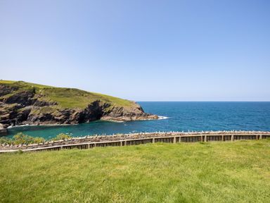 A grassy area with a stone fence overlooking cliffs and the ocean at Gulland in Port Isaac