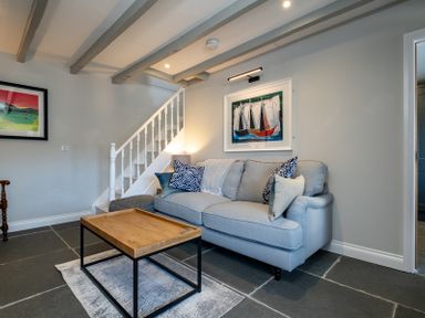 A living room with a light blue sofa and wooden coffee table under exposed ceiling beams at Mino Cottage in Port Isaac