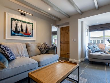 A living room with a sofa a wooden coffee table an armchair and a painting of boats at Mino Cottage in Port Isaac
